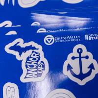 A collection of GVSU themed stickers. The state of Michigan with "Anchor Up" inside, the Laker Up sign, a blue anchor, and GVSU GV logo, and the signature GVSU clocktower